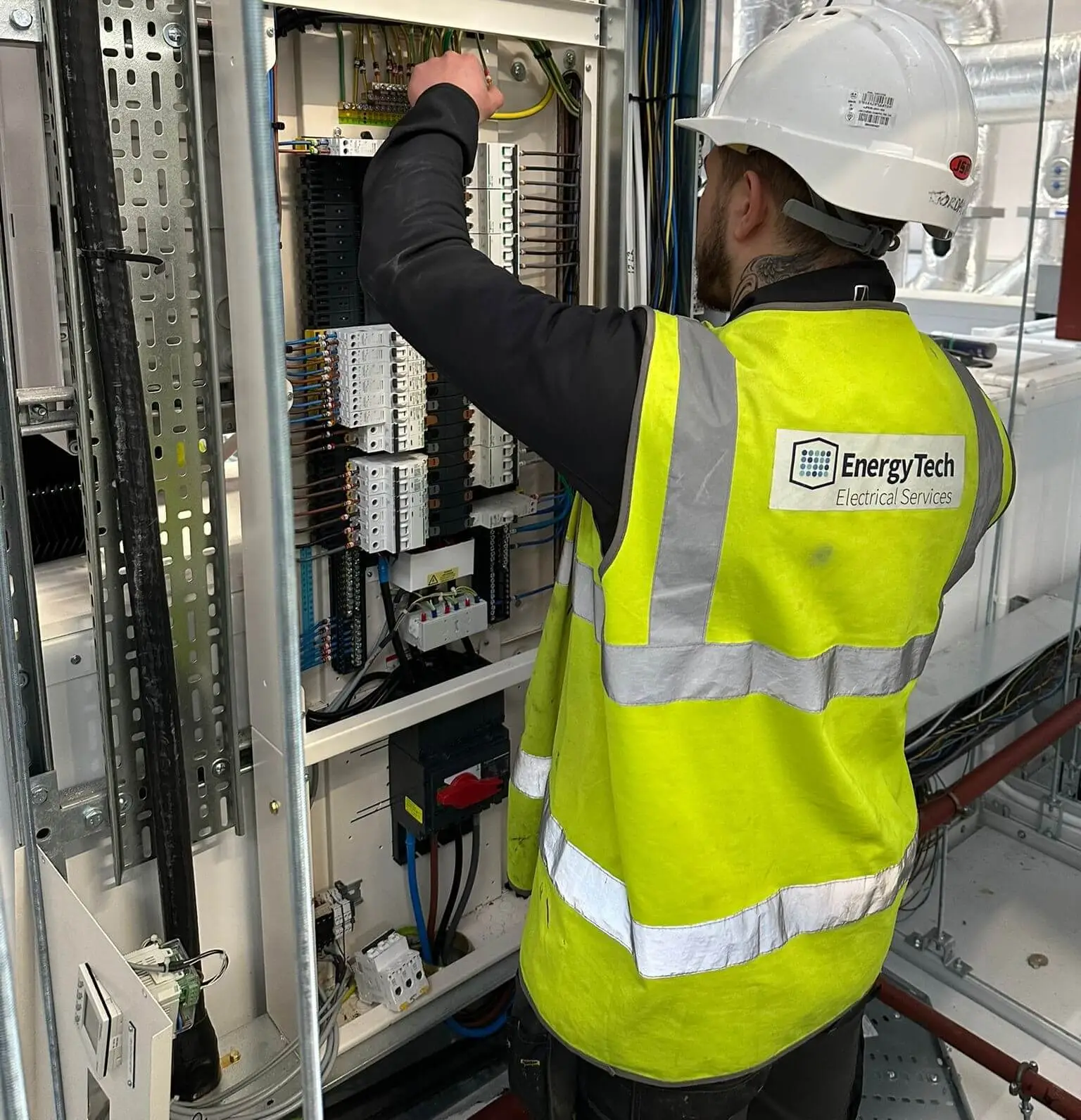 A man in a safety vest is focused on working on an electrical panel